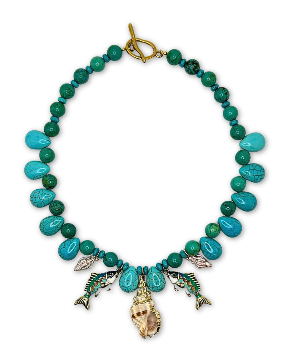 Genuine turquoise beaded fish charm necklace laid flat, with turquoise teardrop beads, enamel fish charms, a shell charm and a gold toggle clasp