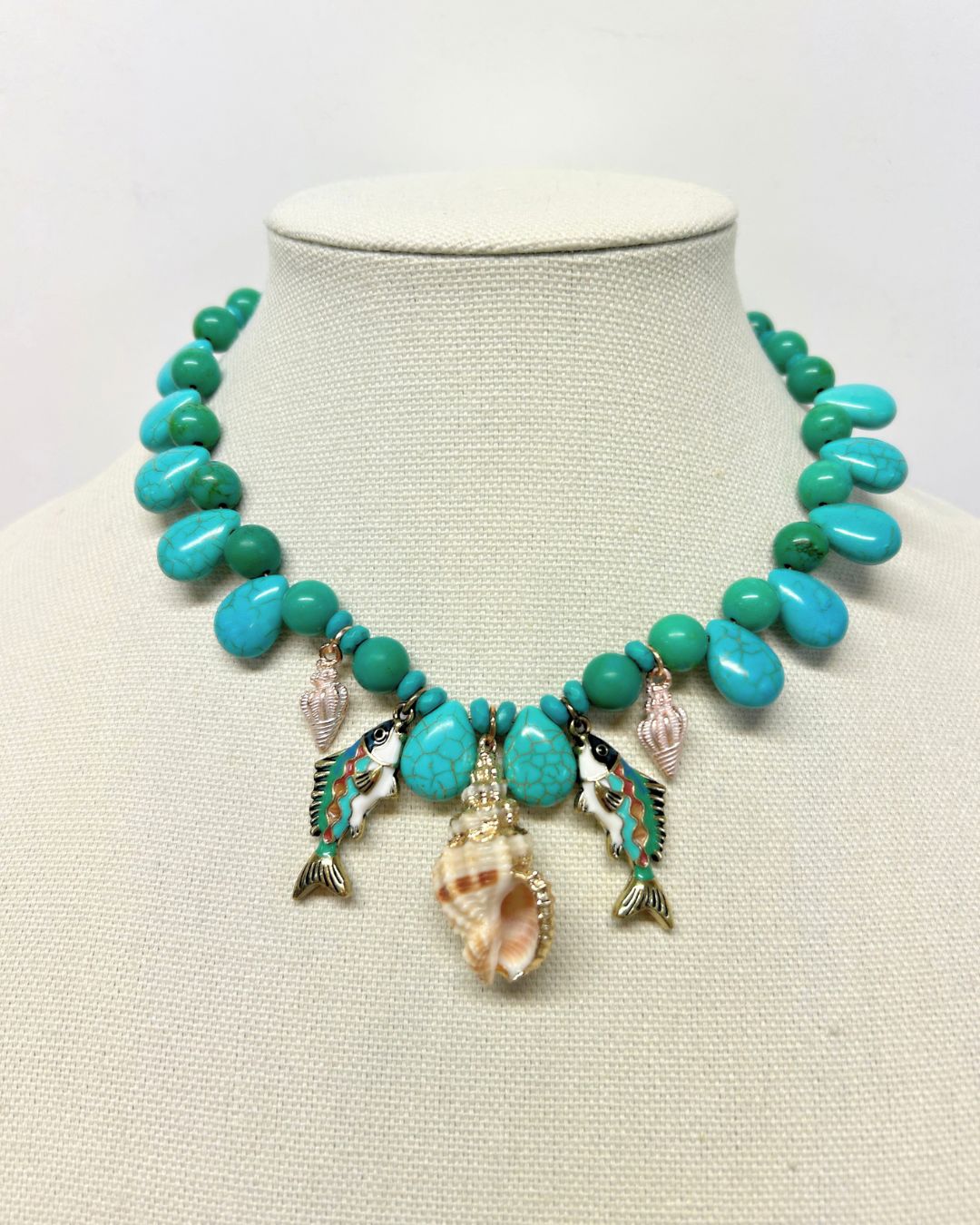 Turquoise beaded fish charm necklace displayed on a linen neck form