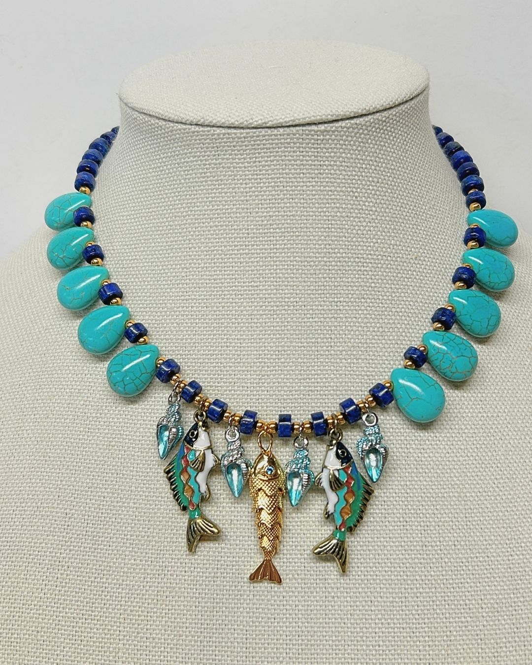 Turquoise howlite and faux lapis fish charm necklace on a linen neck form